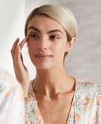 Person with a blonde pixie cut looking in the mirror touching her hand to her eyebrow